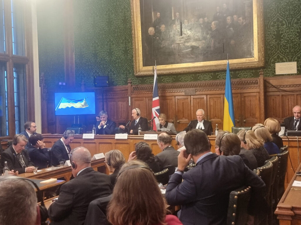 Olena Zelenska speaks to a room of MPs with the UK and Ukrainian flags behind her. 