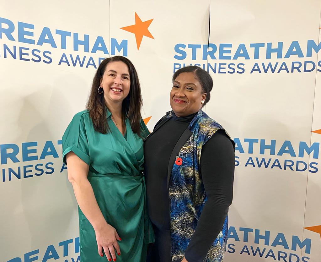 Bell with a business leader in front of a banner that reads Streatham Business Awards. 