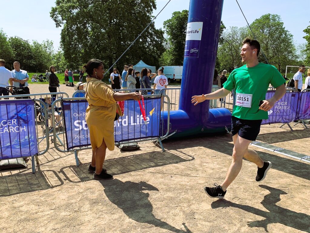 Bell hands out a medal to a runner in a green t-shirt as he passes the finish line