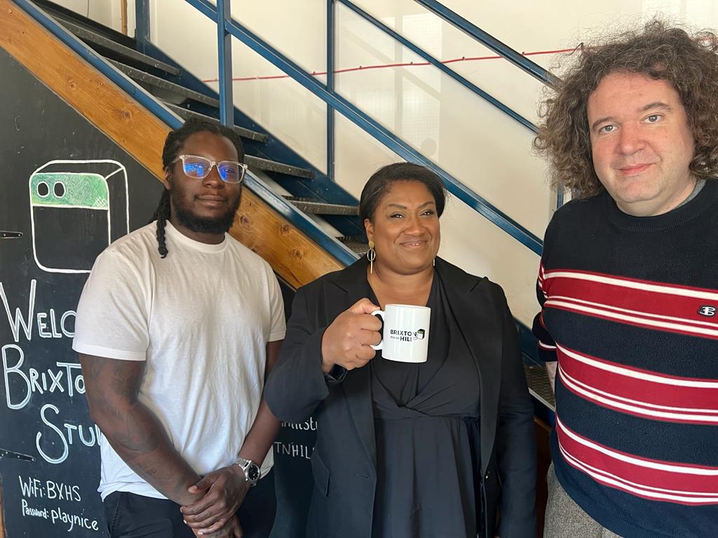 Bell stands holding a Brixton Hill Studios mug with the team